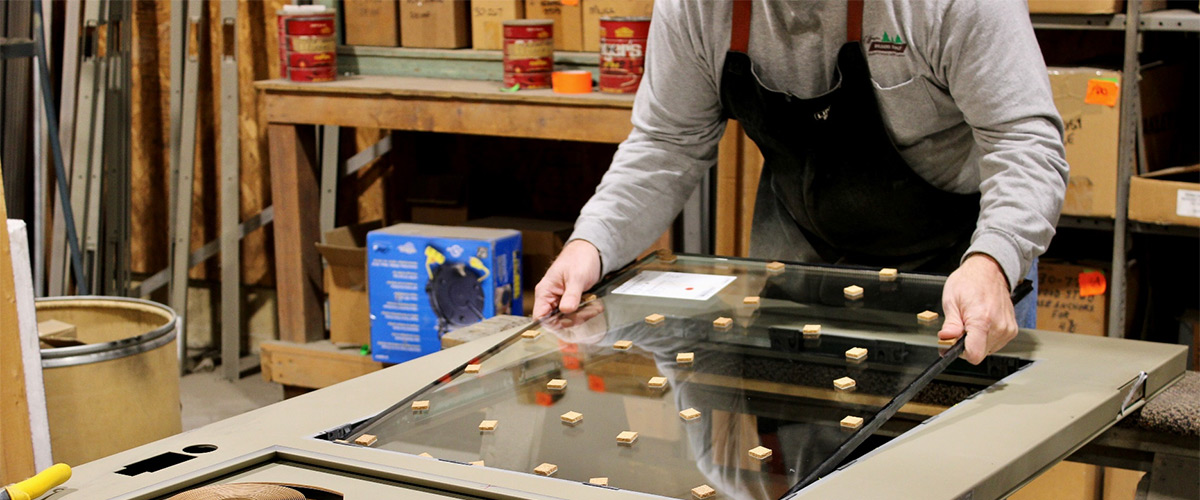 worker placing window glass inside a metal door